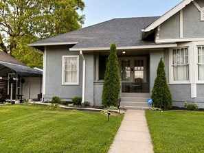 A two-story house with a grey exterior, a front porch, and two tall, conical trees. - Historic Downtown Duplex - Fire Pit, Gym & Parking (Indianapolis)