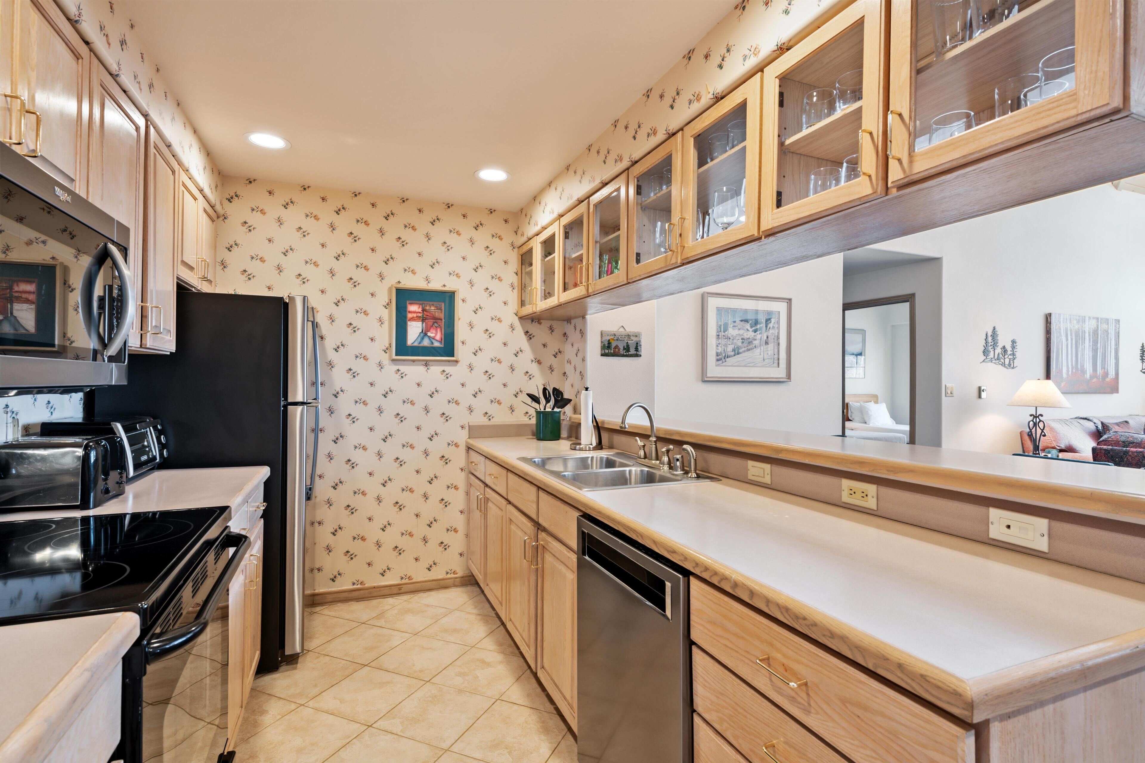 A kitchen with wooden cabinets, a black refrigerator, a dishwasher, and a countertop with a sink.