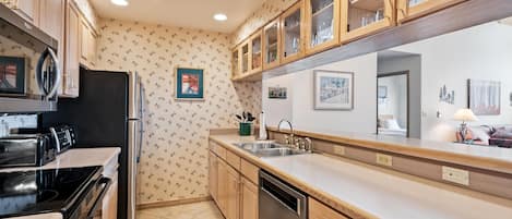 A kitchen with wooden cabinets, a black refrigerator, a dishwasher, and a countertop with a sink.