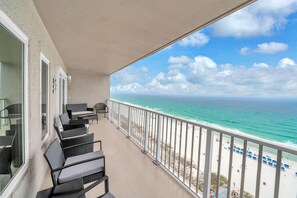 Ein Balkon mit Korbmöbeln, Blick auf den Ozean und ein Strand mit Sonnenschirmen.