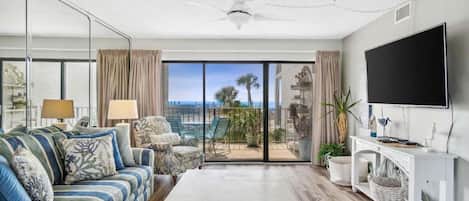 A living room with a sofa, coffee table, TV, and a balcony with a view.