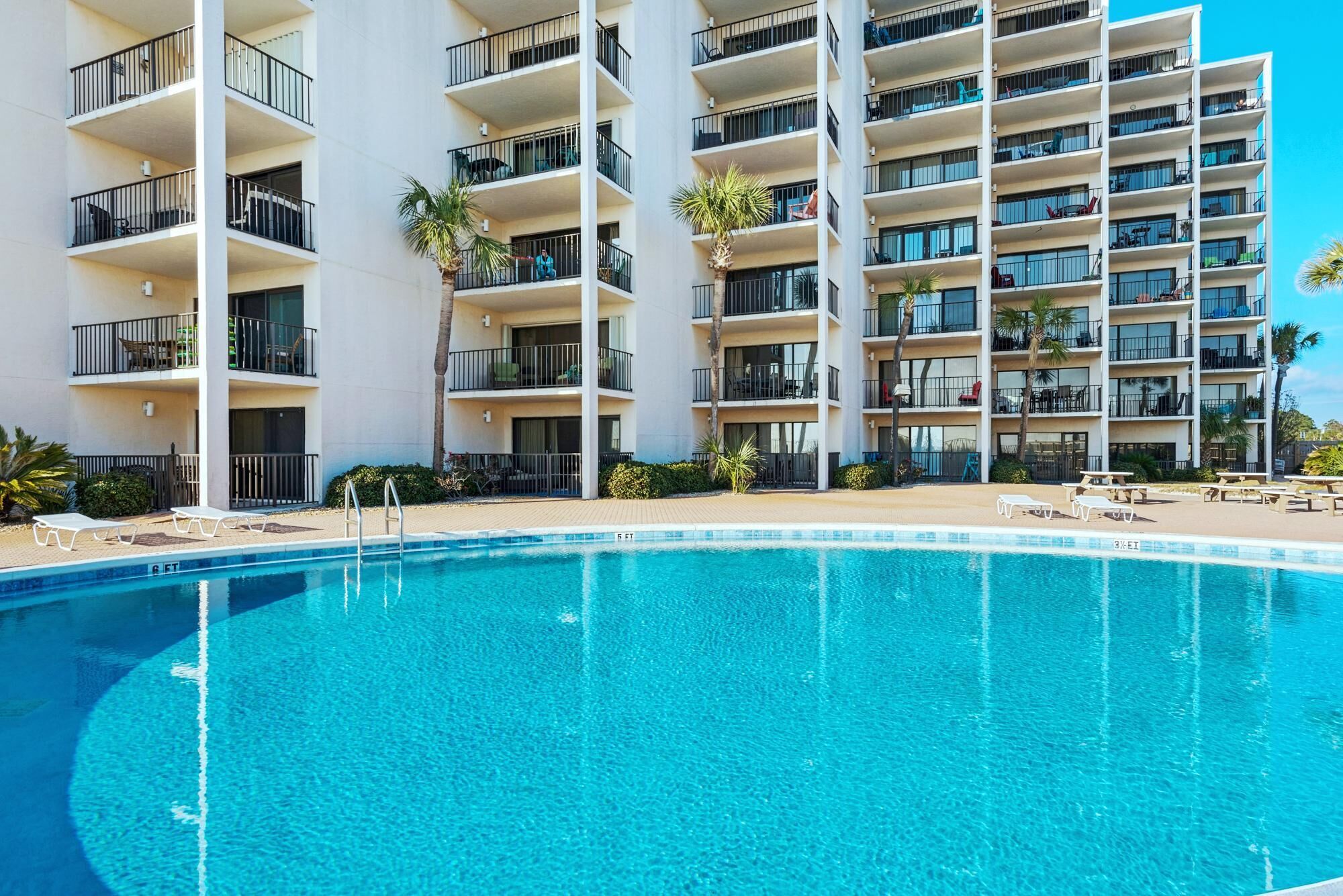 A hotel with a swimming pool, multiple balconies, and outdoor seating areas.