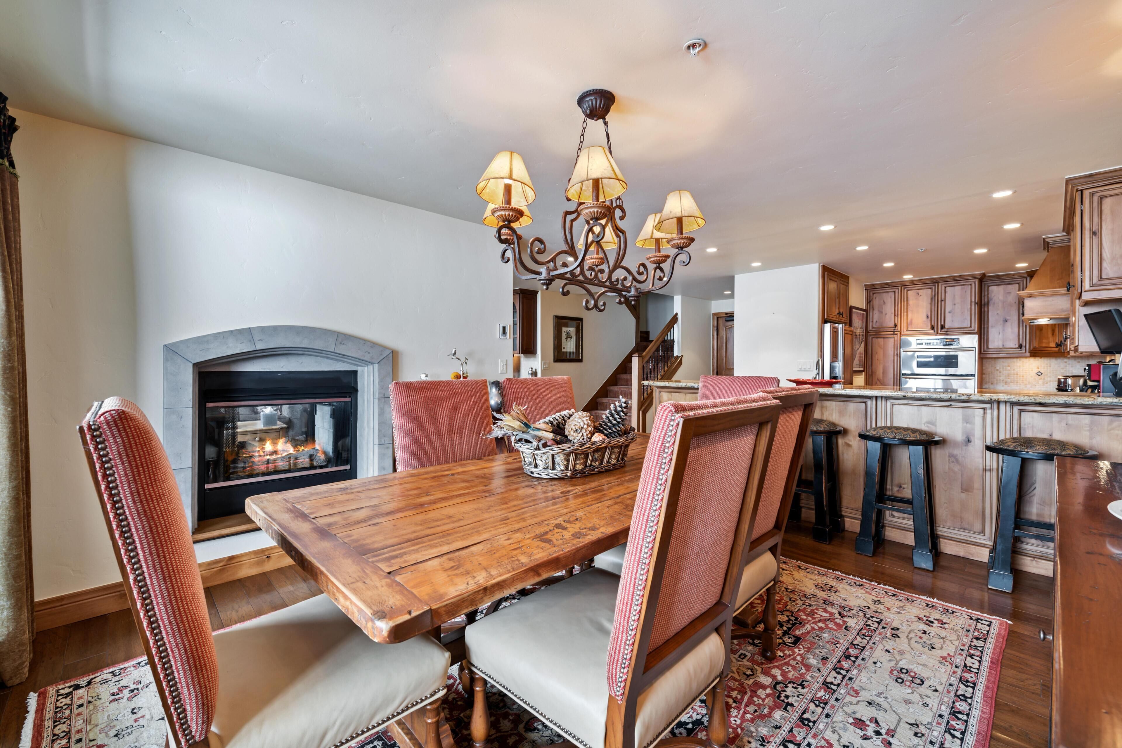 A dining area with a wooden table, chairs, a chandelier, and a fireplace.