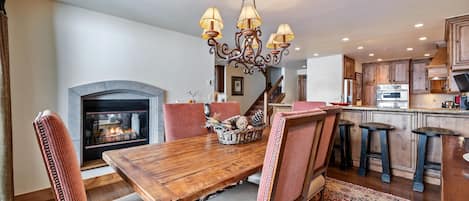 A dining area with a wooden table, chairs, a chandelier, and a fireplace.