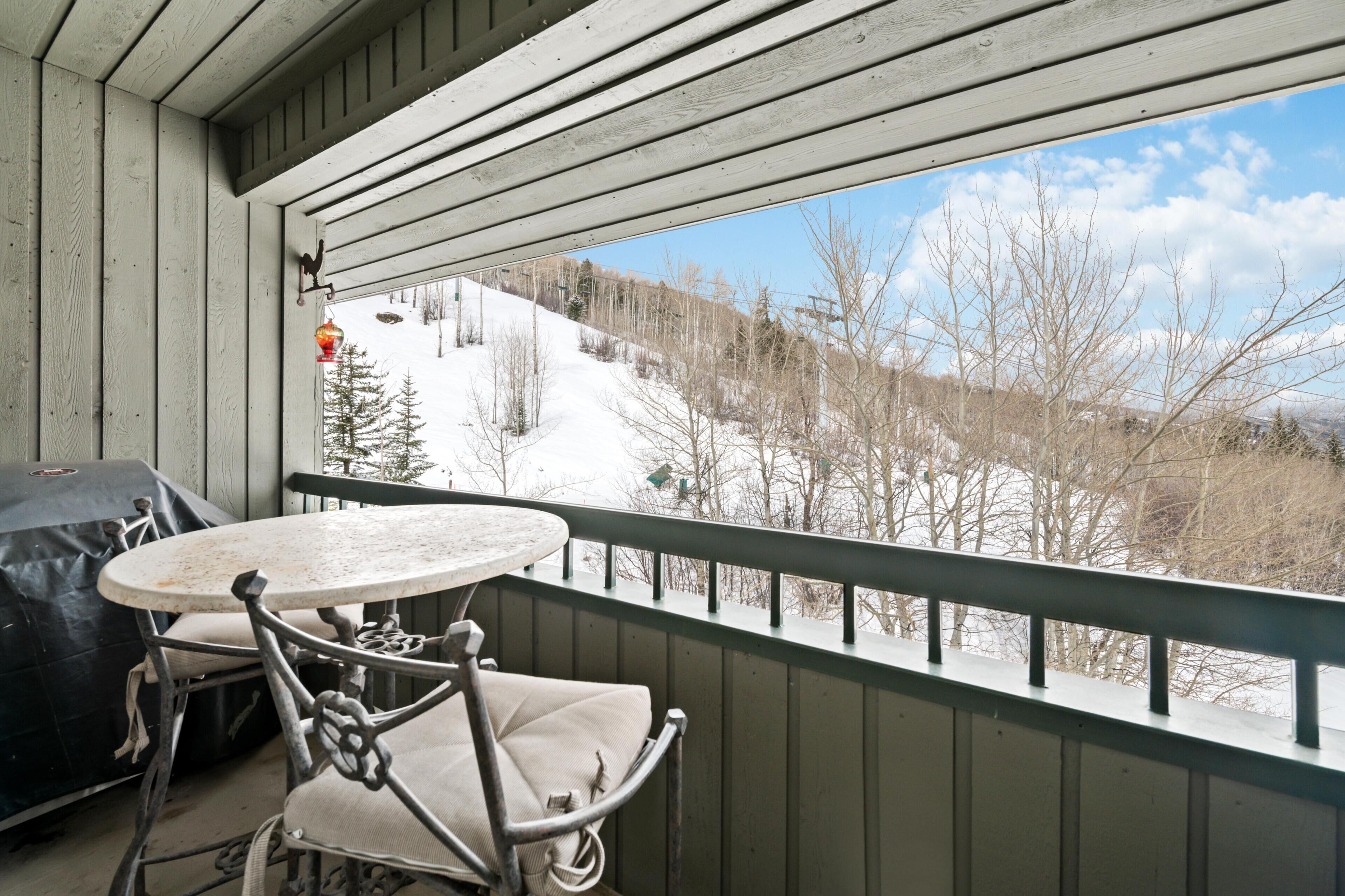A balcony with a table and chairs, overlooking a snowy landscape with trees and a clear sky.
