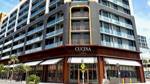A multi-story hotel with balconies, a storefront labeled 'Cucina,' and a pedestrian crossing sign. - Luxury Designer Retreat in Wynwood / Skyline. 2BR. Pool & Bar (Miami)