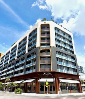 A multi-story hotel with balconies, a storefront labeled 'Cucina,' and a pedestrian crossing sign. - Luxury Designer Retreat in Wynwood / Skyline. 2BR. Pool & Bar (Miami)