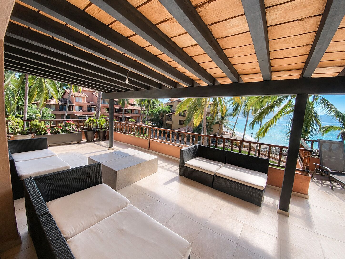 A covered outdoor seating area with wicker furniture, a view of the ocean, and a building in the background.