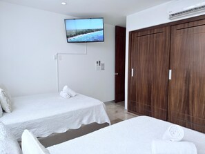 Ein Hotelzimmer mit zwei Betten, einem an der Wand montierten Fernseher, einem Kleiderschrank und einer Klimaanlage.