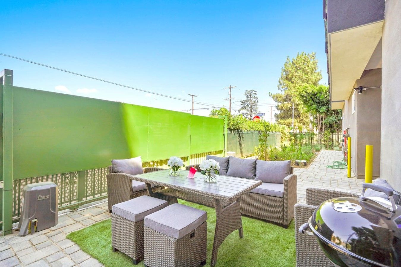 An outdoor patio with wicker furniture, a grill, and a green wall.