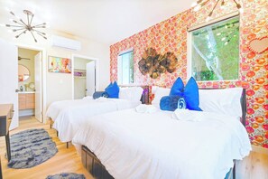Ett hotellrum med två sängar, ett stort fönster, en spegel och en blommig tapet.