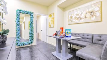 Een moderne woonkamer met een grijze bank, een salontafel met boeken en een gezelschapsspel, een decoratieve spiegel en een bloemig kunstwerk aan de muur.