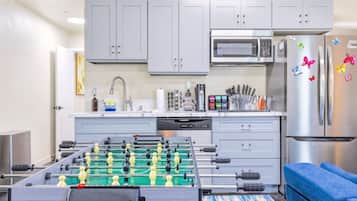Een moderne keuken met grijze kastjes, een tafelvoetbaltafel, een magnetron en een koelkast versierd met kleurrijke magneetjes.