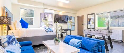 A hotel room with a bed, blue sofas, a foosball table, and a TV.
