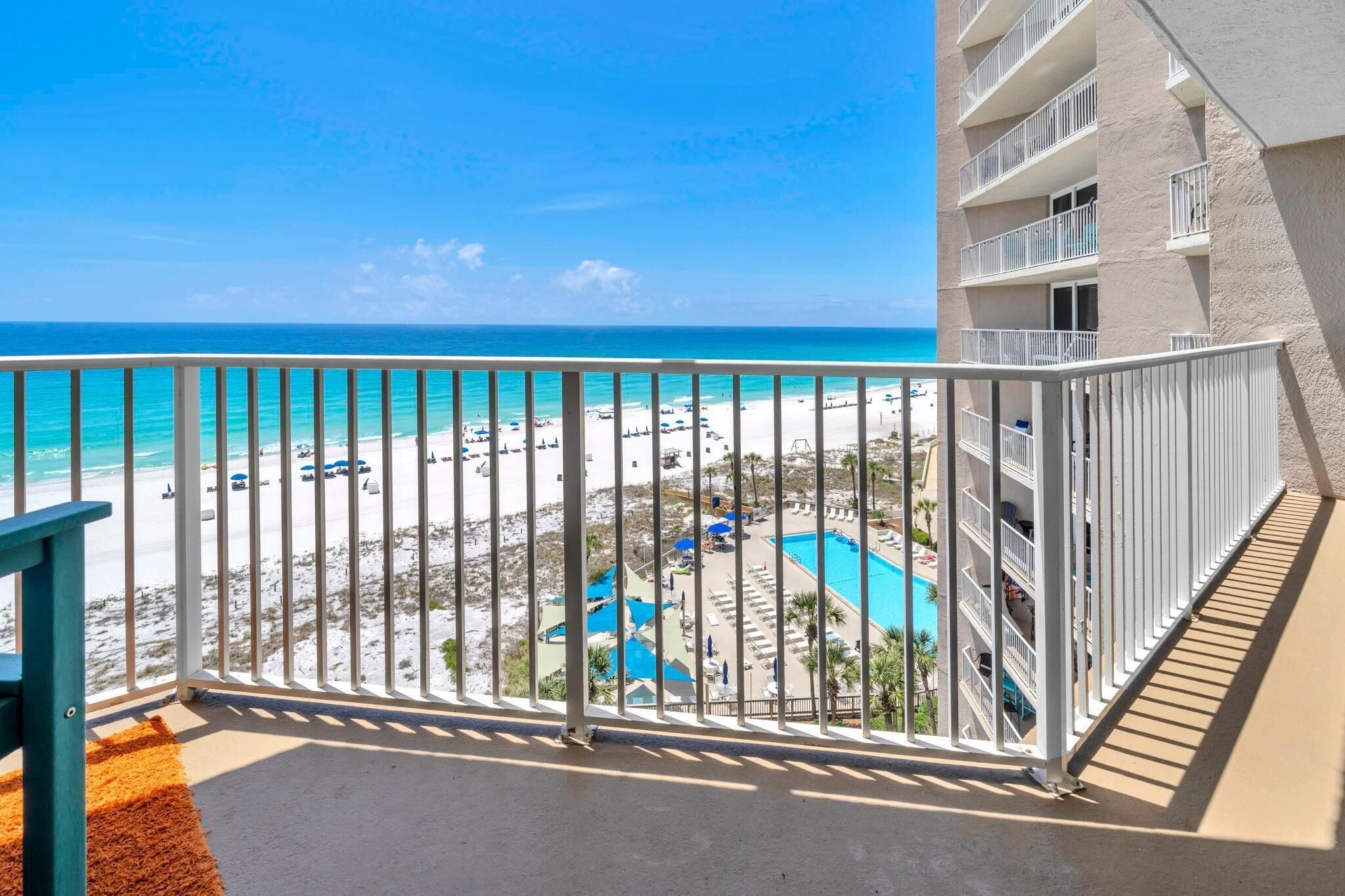 Un balcon donnant sur une plage, une piscine et un immeuble doté de nombreux balcons.