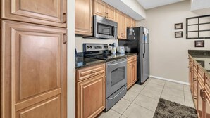 A kitchen with wooden cabinets, stainless steel appliances, and a tiled floor. - Dunes of Panama 904e (Panama City Beach)