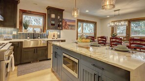 A modern kitchen with a large island, built-in appliances, and a dining area with wooden chairs.
