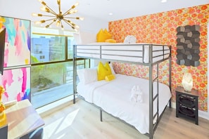 Une chambre avec des lits superposés offrant une vue sur la ville, un lustre moderne et un mur décoré de motifs floraux colorés.
