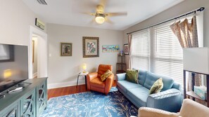 Ein Wohnzimmer mit Fernseher, Deckenventilator, Sofa, Sessel und einem gemusterten Teppich.