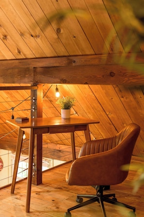 Eine Holzbalkendecke, ein Holztisch mit Topfpflanze und ein Ledersessel in einem Raum mit geneigter Decke.