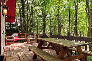A wooden deck with picnic tables and benches, surrounded by trees. - Little Red Chalet | Hot tub, Projector, Fire Pit (Pocono Summit)