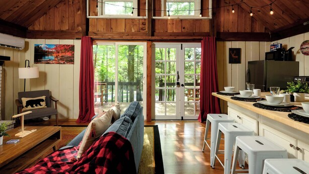 Interior acogedor de una cabaña con sala de estar, cocina y grandes puertas correderas que dan a una terraza.