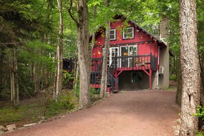 A red wooden cabin with a staircase leading to the entrance, surrounded by trees. - Little Red Chalet | Hot tub, Projector, Fire Pit (Pocono Summit)