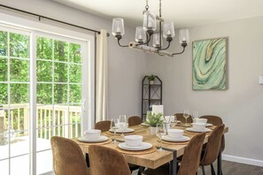 Ein Esszimmer mit großem Tisch für sechs Personen, einer Kristallleuchtre und Blick durch eine Glastür auf eine Terrasse.