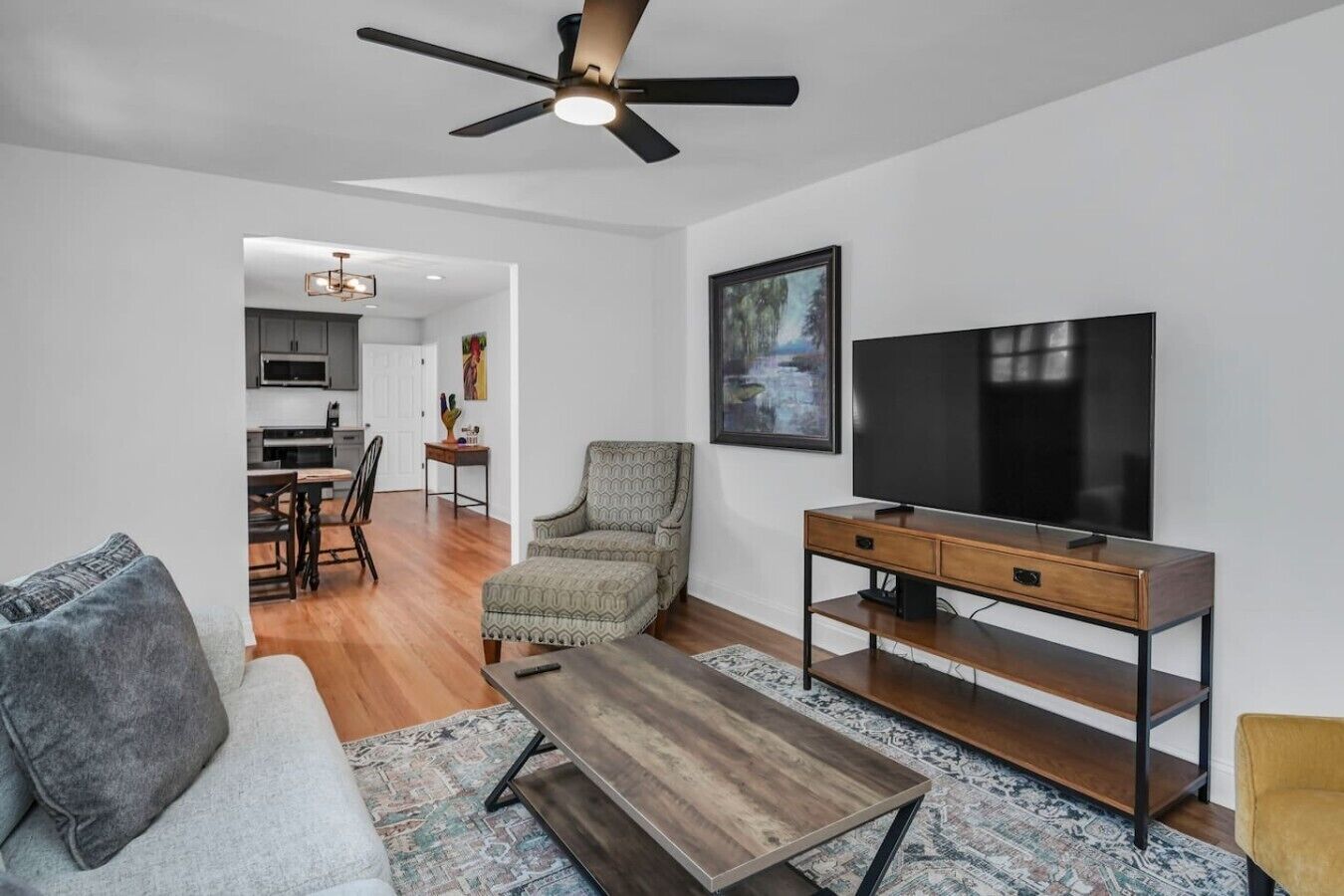 Ein Wohnzimmer mit Sofa, Sesseln, einem Fernsehschrank und einem Deckenventilator.