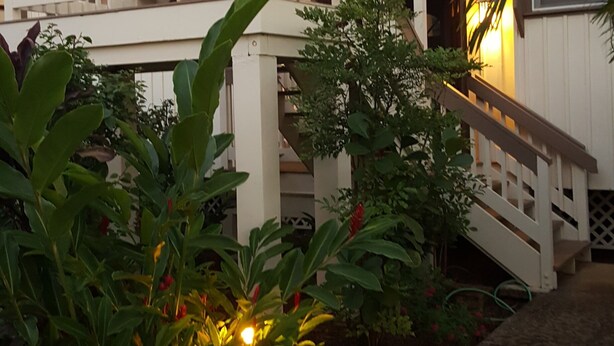 A multi-story building with a white exterior, a balcony, and a staircase leading to the upper levels. - Aloha Hideaways- Palm Retreat A (Princeville)