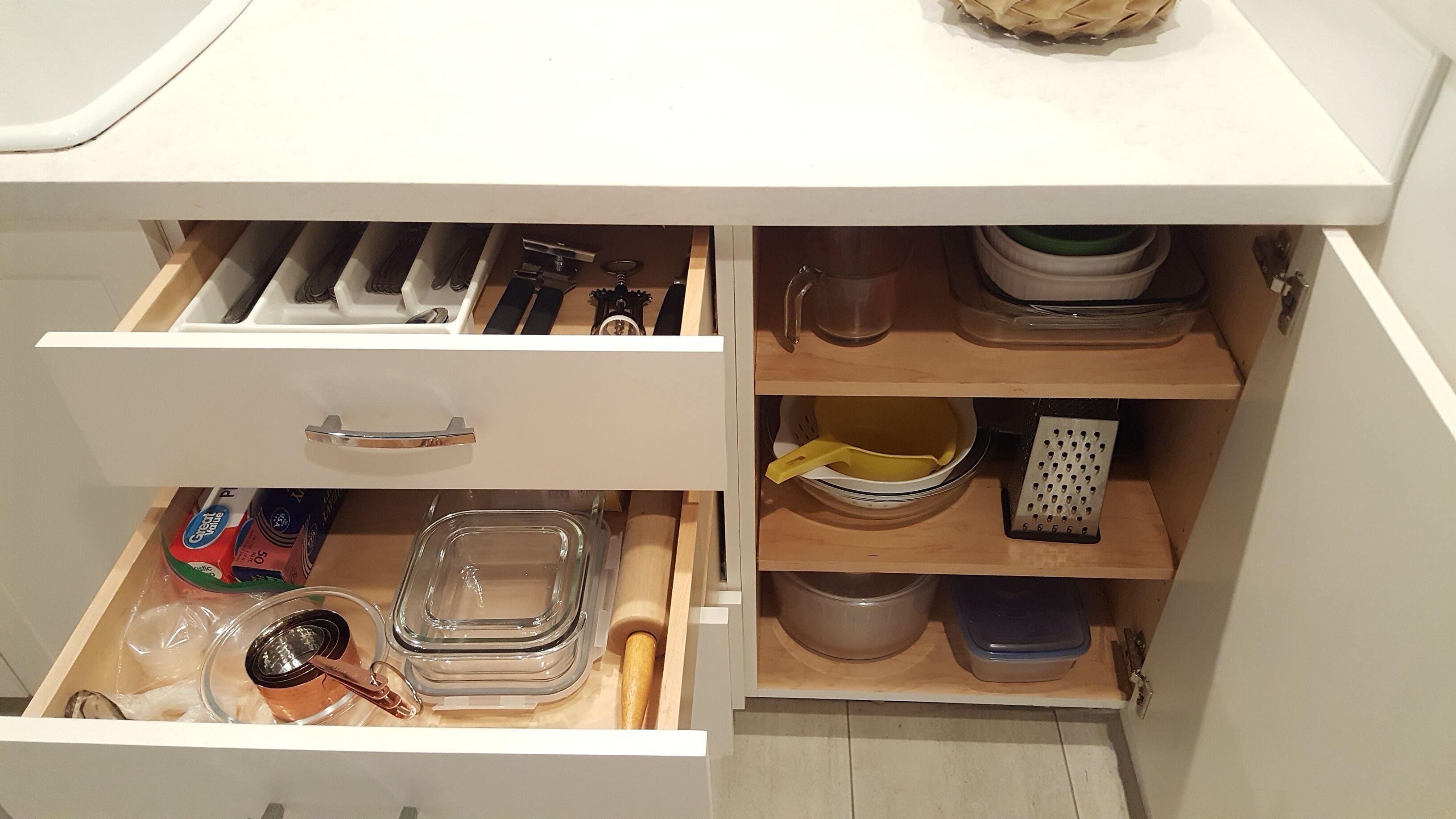 Uma gaveta de cozinha com utensílios, um rolo de massa e um recipiente de vidro.