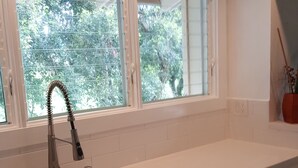 A kitchen with a white countertop, a sink, and a window with a view of greenery. - Aloha Hideaways- Palm Retreat A (Princeville)