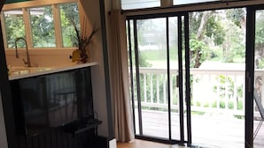 A room with a fireplace, a dining table, a sofa, and a view of a garden through large sliding doors. - Aloha Hideaways- Palm Retreat A (Princeville)
