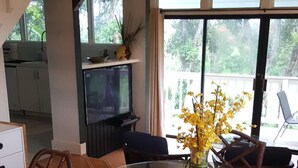 A dining area with a glass table, wooden chairs, a vase with yellow flowers, and a ceiling fan. - Aloha Hideaways- Palm Retreat A (Princeville)