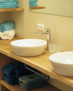 Ein Badezimmer mit einem weißen Waschbecken, einem Spiegel und einem Holzregal mit gefalteten Handtüchern.