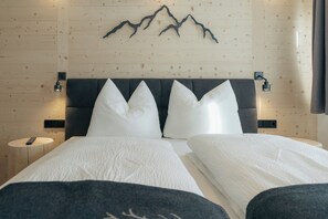 Ein Doppelbett mit weißer Bettwäsche, ein dunkles Kopfteil und Wanddekoration mit Bergmotiven.