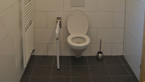 A small, clean bathroom with white tiles, a toilet, a hand dryer, and a plunger. - Apartment on the first floor. (Rosenbach)