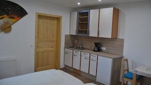 A compact kitchen with a wooden door, white cabinets, a sink, and a small table with a chair. - Apartment on the first floor. (Rosenbach)