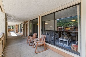 A covered outdoor seating area with wooden chairs and a glass wall providing a view of the landscape. - Vail Village Condo | Walk to Village & Slopes (Vail)