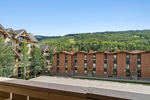 A multi-story building with a brick facade and a flat roof, surrounded by greenery and hills. - Vail Village Condo | Walk to Village & Slopes (Vail)