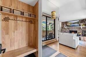 A wooden wall with a coat rack and shelves, a fireplace with a stone mantle, and a view of a balcony with outdoor furniture. - Vail Village Condo | Walk to Village & Slopes (Vail)