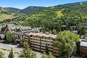 A multi-story hotel with a modern architectural style, located in a mountainous area with dense forest. - Vail Village Condo | Walk to Village & Slopes (Vail)