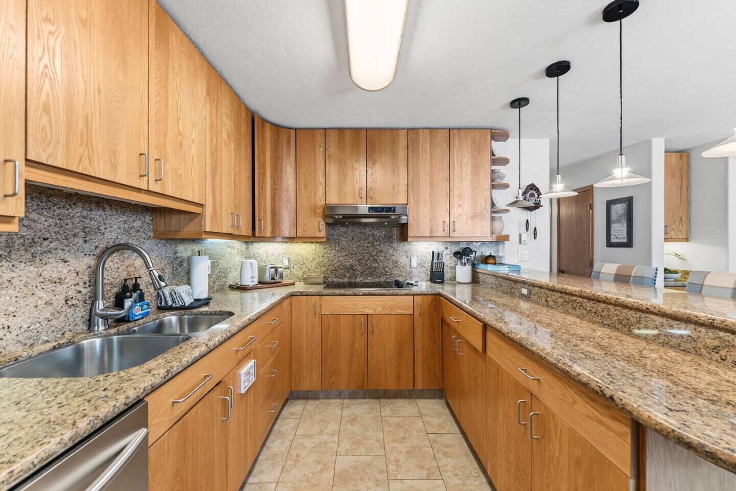 A kitchen with wooden cabinets, granite countertops, stainless steel appliances, and pendant lighting. - Vail Village Condo | Walk to Village & Slopes (Vail)