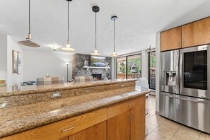 A modern kitchen with granite countertops, wooden cabinets, stainless steel appliances, pendant lighting, and a fireplace. - Vail Village Condo | Walk to Village & Slopes (Vail)
