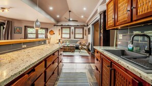 Cucina con mobili in legno, piano di lavoro in granito, ventola a soffitto e finestra con persiane.