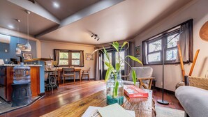 Un soggiorno con pavimento in legno, un divano, un tavolino da caffè con un libro e un vaso, una zona pranzo con tavolo e sedie, e un angolo cucina con un bancone e elettrodomestici.