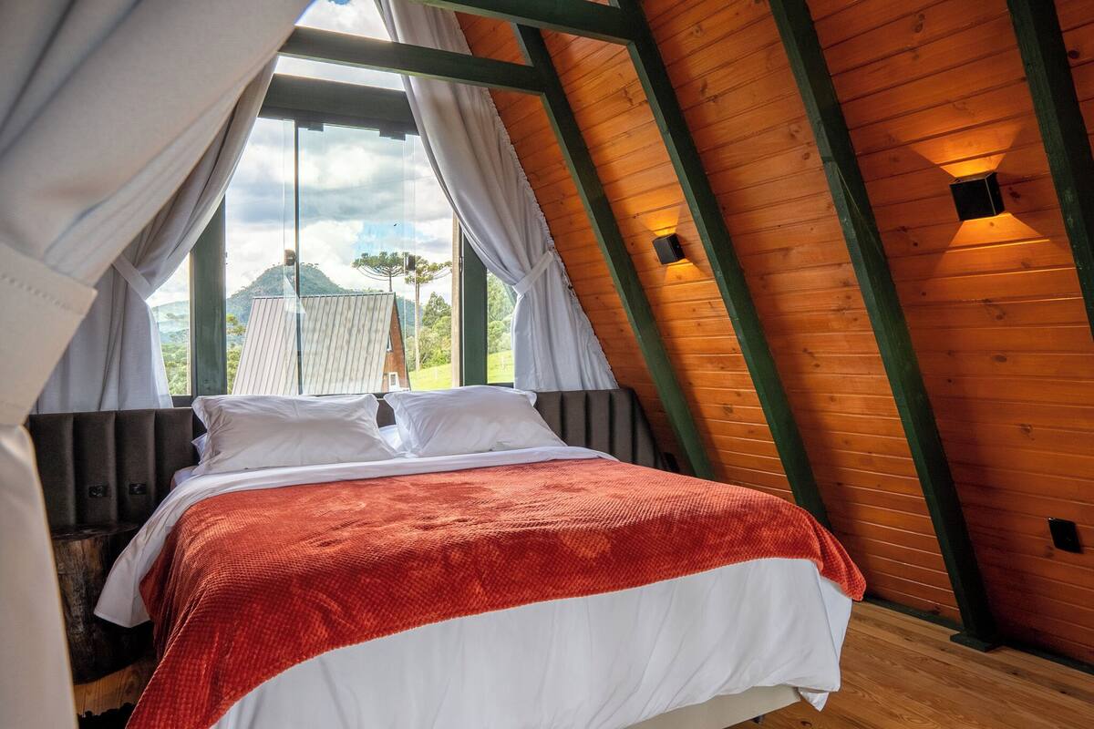 Un dormitorio con cama, cortinas blancas, techo de madera y vistas al exterior.