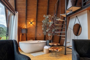 A modern interior with a large bathtub, wooden walls, a staircase, and a potted plant. - Altitude 1140 Chalés (Águas Brancas)