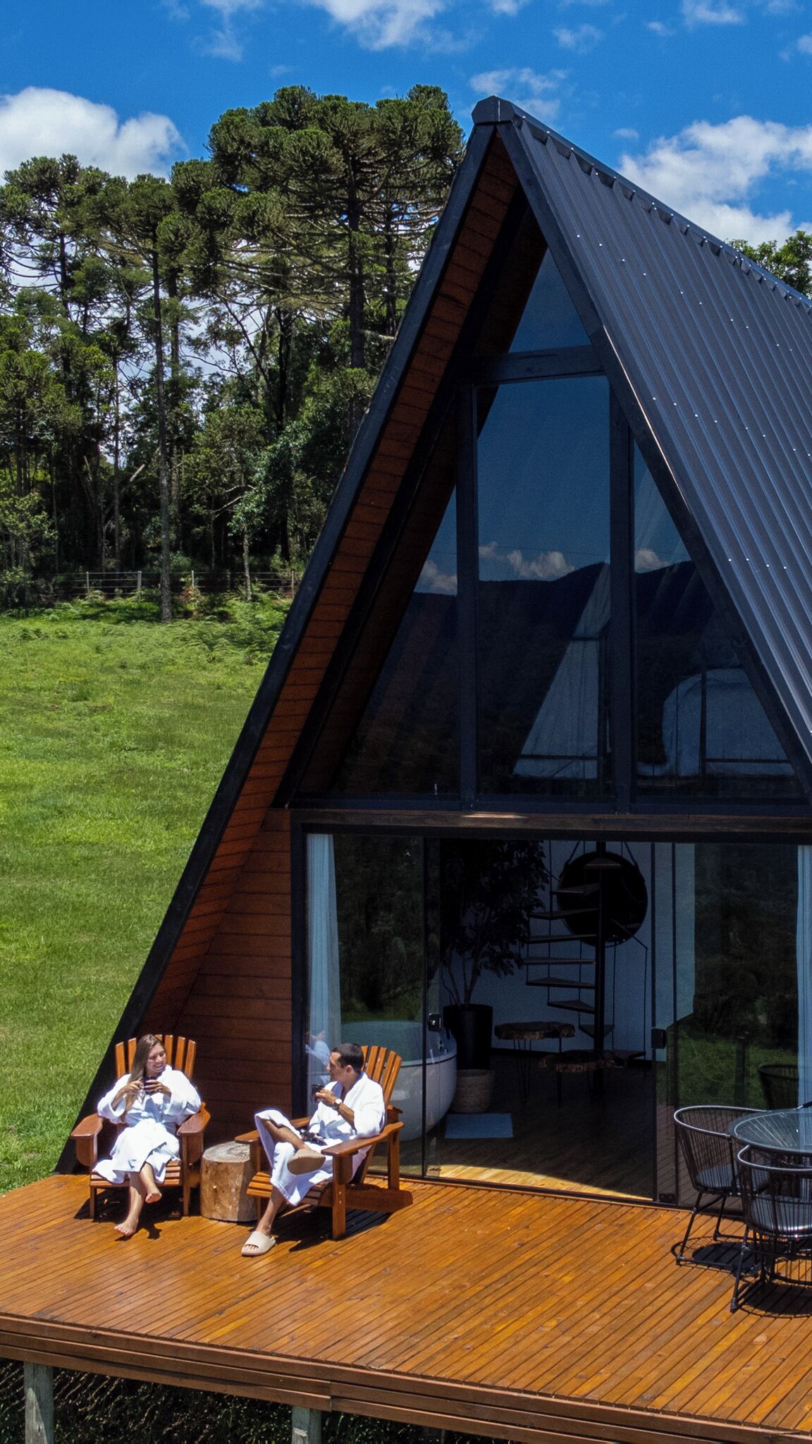 A modern house with a sloped roof, large windows, and a wooden deck with outdoor furniture.