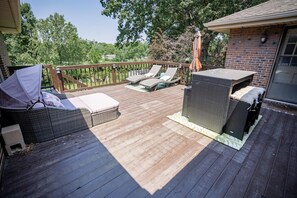 A deck with wicker furniture, a covered seating area, and a view of the surrounding greenery. - 5 Mins to Arrowhead | 3BR KC Retreat | 3 Ensuites, Sauna & Theater (Independence)